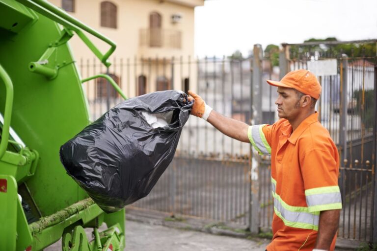 Un operario con mono de trabajo lanza una bolsa de basura al camión de recogida.